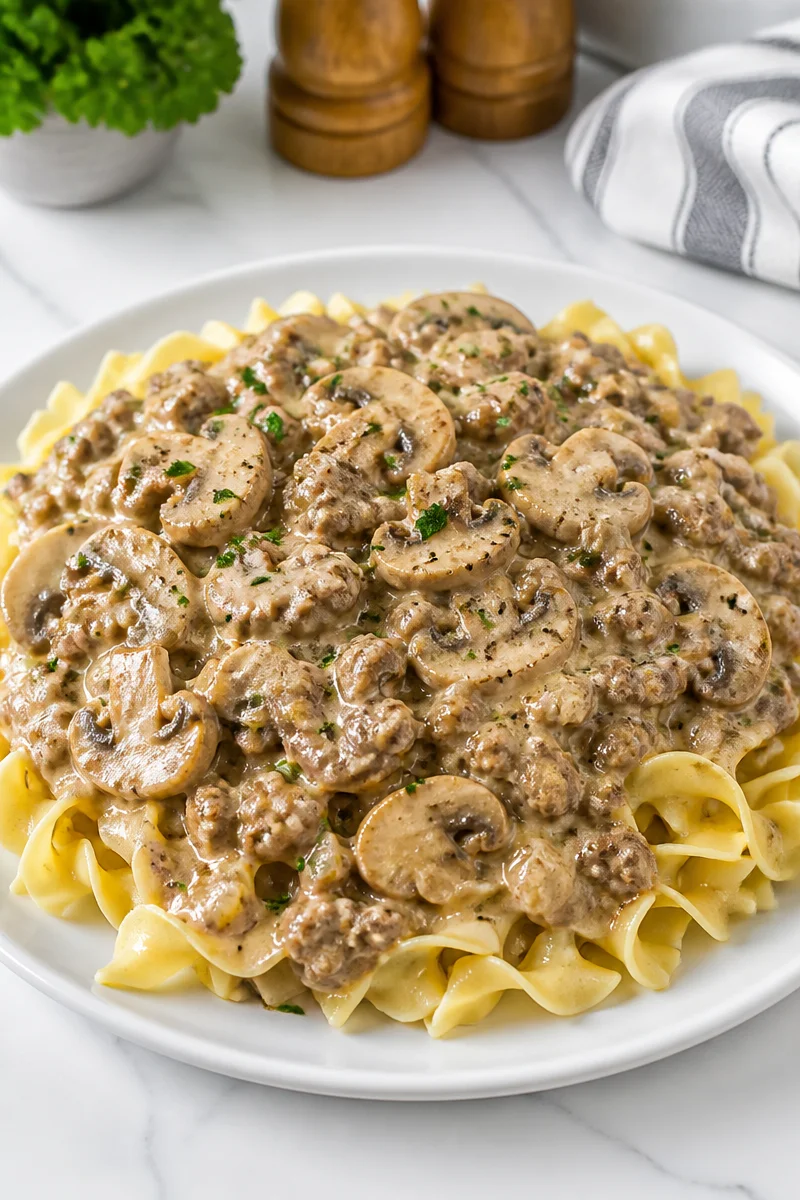 Creamy mushroom and ground beef stroganoff served on a plate with parsley garnish.